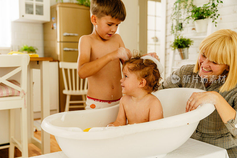 Mother bathing her baby boy in a bathtub in the living room